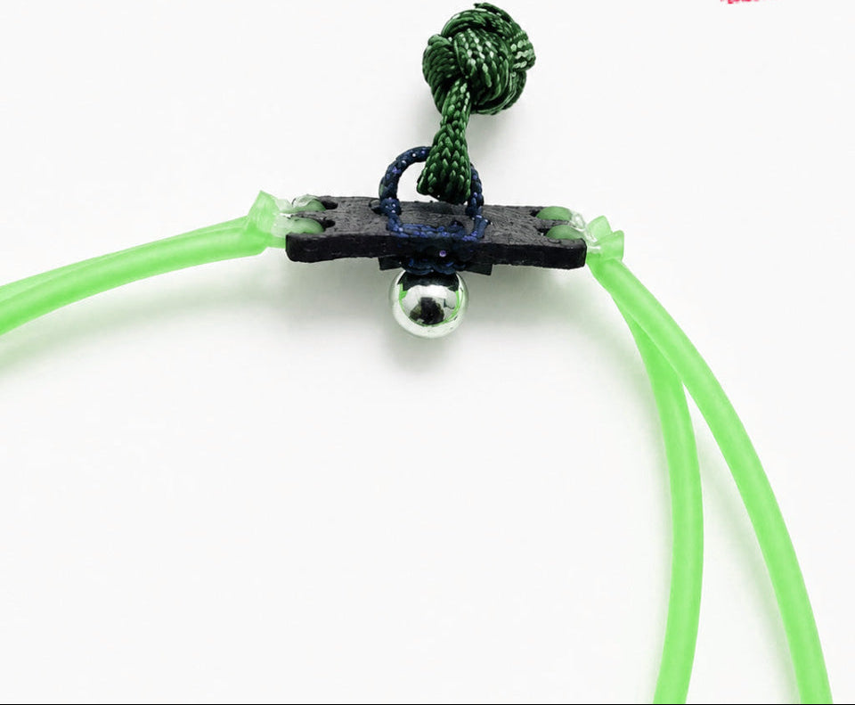Green slingshot with a black anchor and silver ball on a white background, featuring a brand logo in the corner.