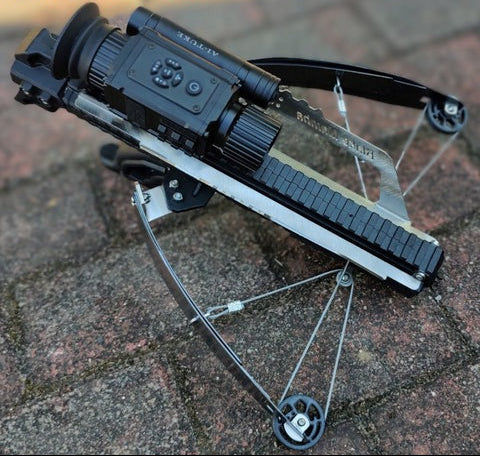 Crossbow with scope on a brick surface.